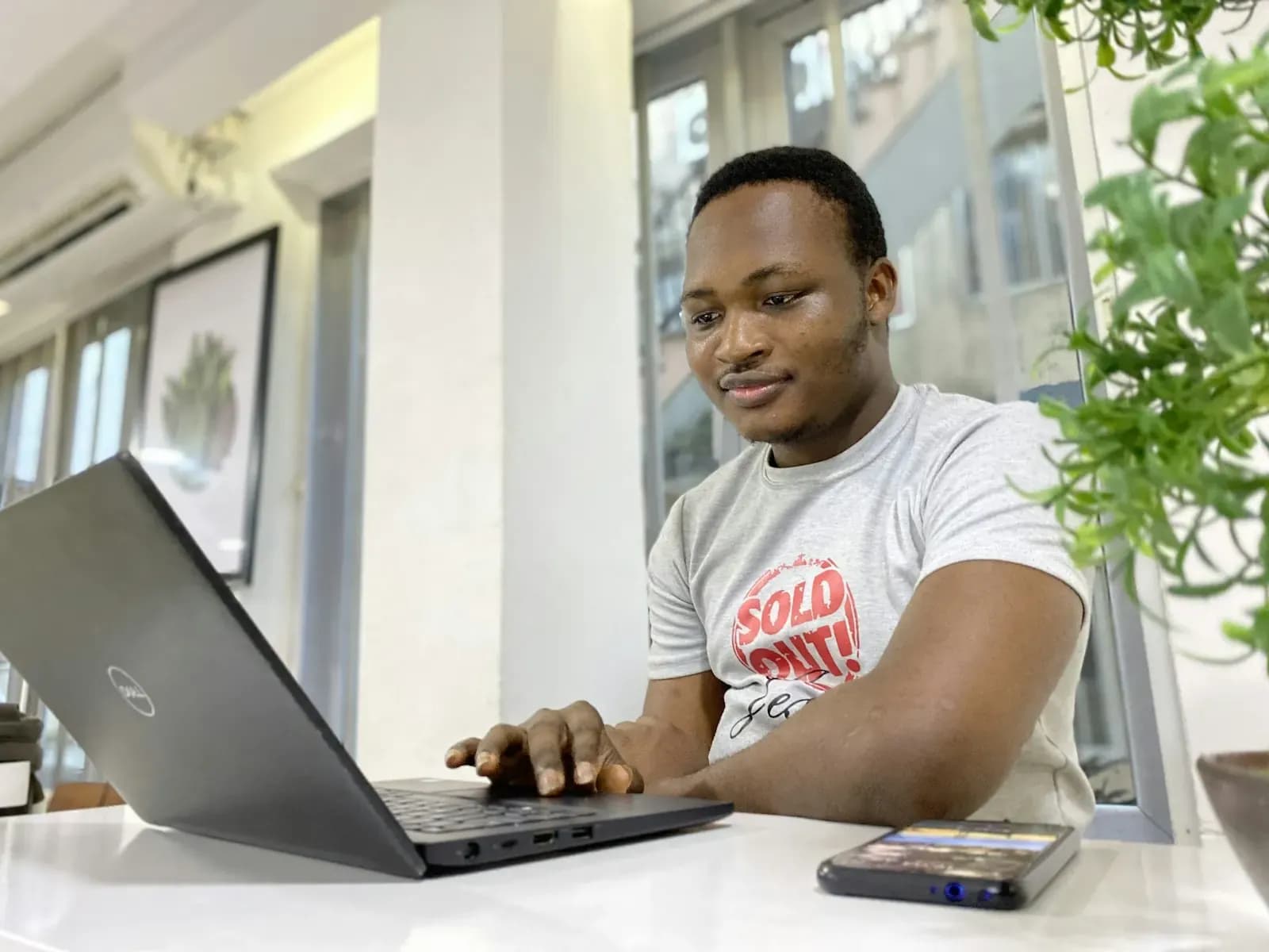 Man smiling while working on a laptop in a bright workspace